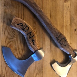 May include: Two wooden-handled axes with metal blades. The handles are engraved with the names "DAN" and "TC".