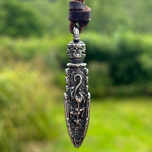 May include: A silver pendant necklace featuring an intricate dragon design. The pendant is shaped like a spearhead and hangs from a brown leather cord.
