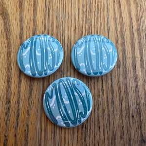 May include: Three blue and white oval buttons with the word "MOIST" written in a stylized font.