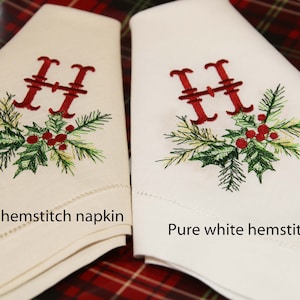 May include: Two embroidered napkins with a Christmas holly and pine design and the letter "H" in red thread. The napkin on the left is dark ivory hemstitch and the napkin on the right is pure white hemstitch.