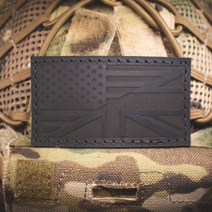 Könnte beinhalten: Ein schwarzer Leder-Patch mit der amerikanischen und britischen Flagge, die zusammengenäht sind. Der Patch ist an einem Tarnhelm befestigt.