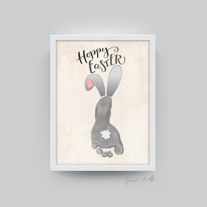 May include: A printable art print featuring a gray bunny footprint with pink ears and a white tail. The text "Hoppy Easter" is written in black cursive above the bunny footprint.