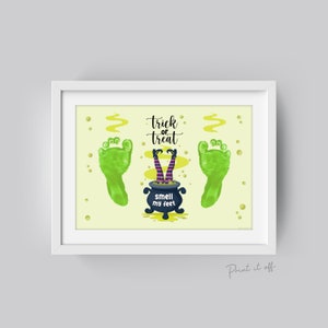 May include: A framed Halloween-themed print with a light yellow background. The print features green footprints, a cauldron with witch legs, and the text "trick or treat" and "smell my feet".