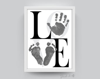 May include: A white framed print with the word "LOVE" in black letters. The "O" is replaced with a gray handprint and the "V" is replaced with two gray footprints.