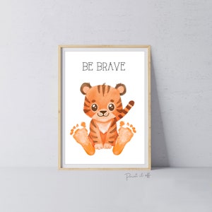 Puede incluir: Una impresión de arte imprimible con una ilustración de acuarela de un lindo cachorro de tigre naranja y negro con sus huellas de patas. El texto "BE BRAVE" está impreso sobre el tigre.