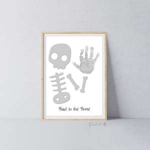 Op de afbeelding: Een afdrukbare kunstprint met een grijs skelet met een handafdruk voor het hoofd. De tekst "Bad to the Bone" is onder het skelet gedrukt.