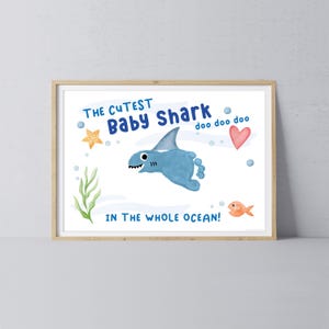 May include: A framed print featuring a blue baby shark illustration made from a footprint, with the text "THE CUTEST Baby Shark doo doo doo IN THE WHOLE OCEAN!" Also includes a starfish, heart, fish, and seaweed.