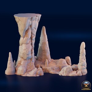 May include: A 3D printed miniature set of rock formations, featuring a tall, pointed spire with a flat top, and several smaller, jagged rocks. The rocks are a light brown color and have a rough, textured surface.