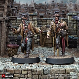 Puede incluir: Dos figuras en miniatura pintadas de hombres con abrigos, sombreros y pantalones marrones. Una figura sostiene una pistola y la otra un bastón. Ambas figuras están de pie sobre bases negras.