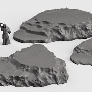 Puede incluir: Tres plataformas rocosas grises, ideales para juegos de mesa o la exhibición de miniaturas. Las plataformas son de varios tamaños y formas, con superficies rugosas y texturizadas.