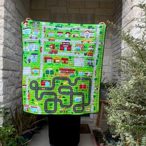 May include: A green and white play mat with a city scene and roads for toy cars. The mat features buildings, cars, and trucks.