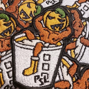 May include: A close-up of several embroidered patches featuring a cartoon pumpkin character holding a cup of coffee. The patches are orange, brown, white, and green.