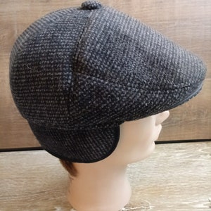 May include: A black and gray tweed newsboy cap with ear flaps. The cap has a button on top and a curved brim.
