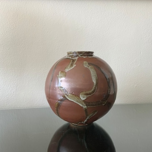 May include: A round, brown ceramic vase with a white glaze. The vase has a unique, abstract design with brown and white lines.