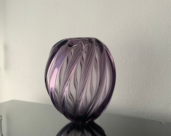 May include: A purple glass vase with a swirling, textured design. The vase is round and has a wide opening.