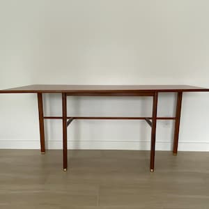 May include: A mid-century modern style wooden console table. The table has a rectangular top and four slender legs with brass-colored tips. The table is 60 inches long, 15 inches wide, and 30 inches tall.