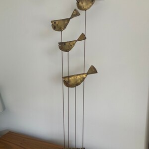 May include: A gold metal sculpture of four stylized fish, each with a different pose, mounted on a stand with multiple metal spikes. The sculpture is on a wooden surface.