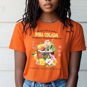 May include: An orange t-shirt with a Piña Colada design. The graphic shows a cocktail in a coconut shell, with flowers and fruit. Text includes "The sweet taste of summer" and "Pina Colada".