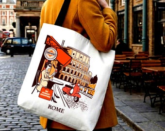 Könnte beinhalten: Eine weiße Stofftasche mit einer grafischen Illustration von Rom, die das Kolosseum, einen roten Roller und eine an einem Cafétisch sitzende Person zeigt. Das Design umfasst eine orangefarbene Markise, ein rundes Logo und eine rote Tasche mit der Aufschrift NO SUNDAY SHOPPING.