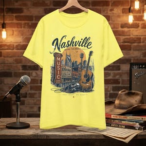 May include: A bright yellow short-sleeve t-shirt featuring a graphic print of the Nashville skyline, an acoustic guitar, a cowboy hat, and the text Nashville Where The Music Lives, Live Music Every Night, Broadway Is Callin, Three Chords One Heart.