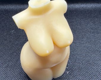 May include: A beige candle shaped like a human torso. The candle has a white wick.