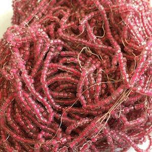 May include: A large pile of pink glass seed beads. The beads are small and round, and they are strung together on a thin thread.