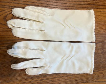 Könnte beinhalten: Ein Paar cremeweiße Handschuhe in Handgelenklänge mit einem gewellten Rand an der Öffnung und drei dekorativen Ziernähten auf dem Handrücken. Die Handschuhe sind mit sichtbaren Nähten entlang der Finger gearbeitet.