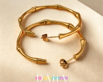 May include: A pair of large gold hoop earrings with a bamboo-inspired design. The earrings are made of metal and have a polished finish.