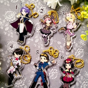 May include: A collection of six acrylic character keychains. Each keychain features a different anime-style character with unique outfits and accessories. The keychains are attached to gold-colored ball chains.
