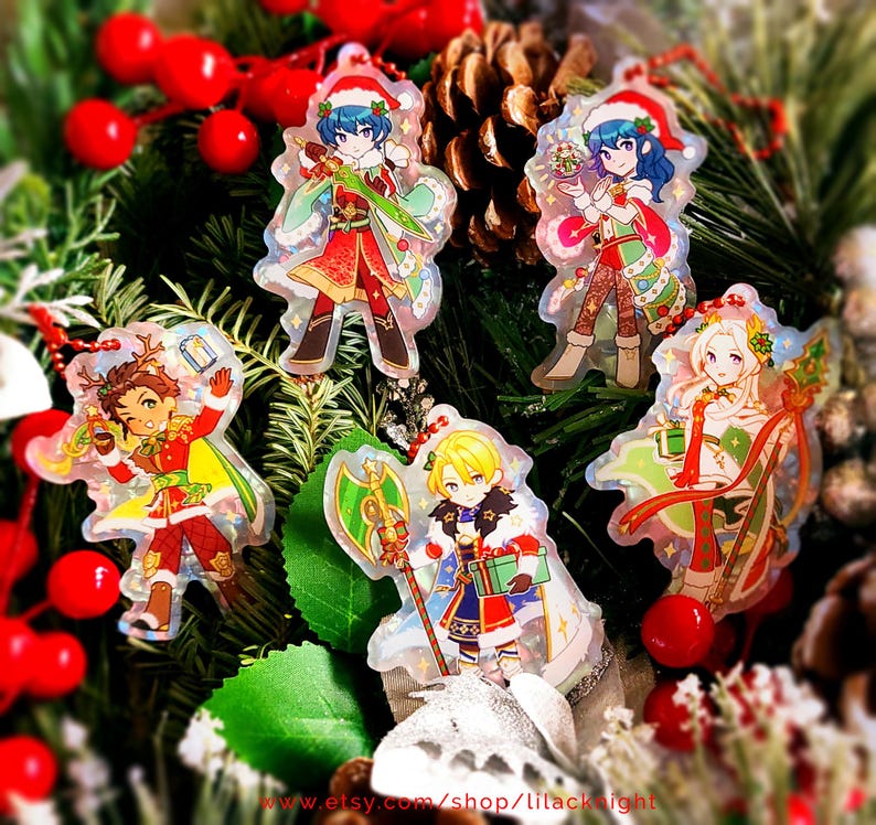 May include: A collection of five Christmas-themed acrylic charms featuring anime-style characters in festive outfits. The charms are clear with colorful designs, set against a backdrop of Christmas greenery and red berries. Each charm has a red string for hanging.