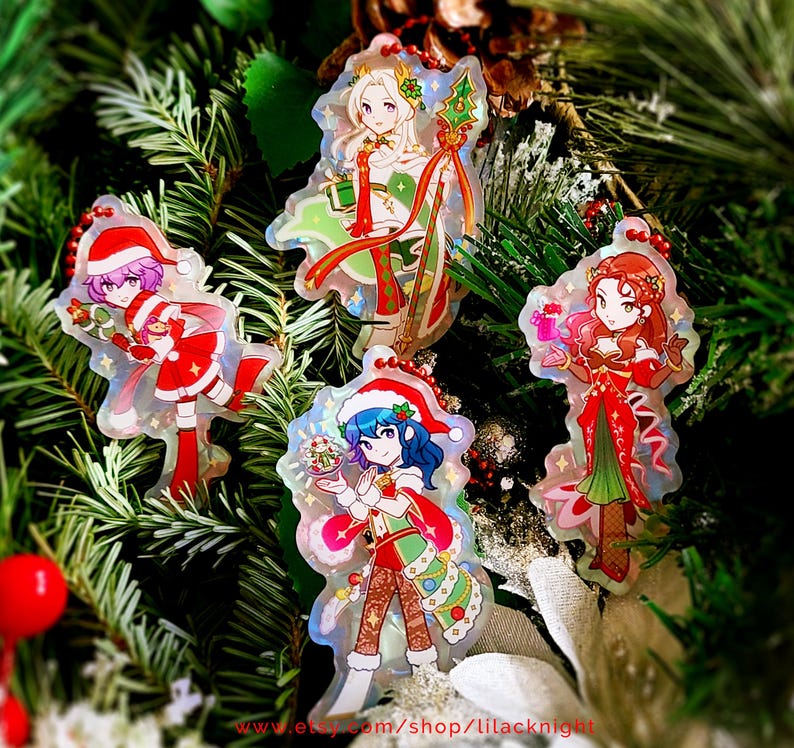 May include: Four Christmas-themed anime character acrylic charms with red, green, and white outfits and Santa hats. The charms are hanging on a Christmas tree with green needles and red berries.