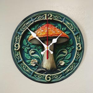 May include: Round wall clock featuring a detailed mushroom design. The clock face has a dark teal background with a large orange and white mushroom in the center. White clock hands point to the time. The clock is a decorative home decor item.