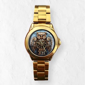 K&ouml;nnte beinhalten: Goldfarbene Armbanduhr mit Eulen-Design. Das Zifferblatt zeigt eine detaillierte Eulenillustration mit mechanischen Fl&uuml;geln und r&ouml;mischen Ziffern. Die Uhr hat ein goldenes Armband und ein rundes Zifferblatt.
