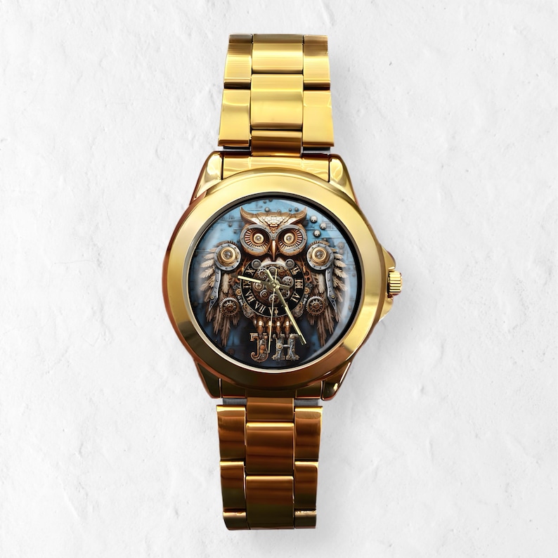 K&ouml;nnte beinhalten: Goldfarbene Armbanduhr mit Eulen-Design. Das Zifferblatt zeigt eine detaillierte Eulenillustration mit mechanischen Fl&uuml;geln und r&ouml;mischen Ziffern. Die Uhr hat ein goldenes Armband und ein rundes Zifferblatt.