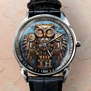 K&ouml;nnte beinhalten: Silberne Armbanduhr mit schwarzem Lederarmband. Das Zifferblatt zeigt ein detailliertes Steampunk-Eulen-Design mit Zahnr&auml;dern und blauem Hintergrund. Die L&uuml;nette hat schwarze Markierungen. Die Uhr hat ein silbernes Geh&auml;use.
