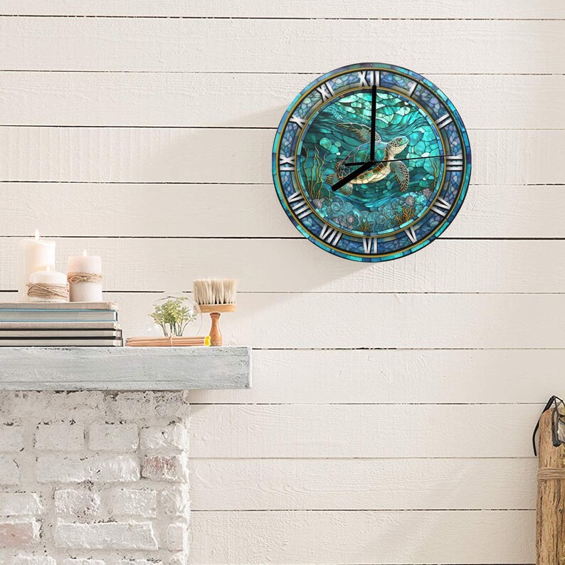 May include: Circular wall clock featuring a sea turtle design. The clock face depicts a teal and blue underwater scene with a swimming turtle. Roman numerals mark the hours, and the clock has a gold-coloured rim. It is mounted on a white wooden wall.