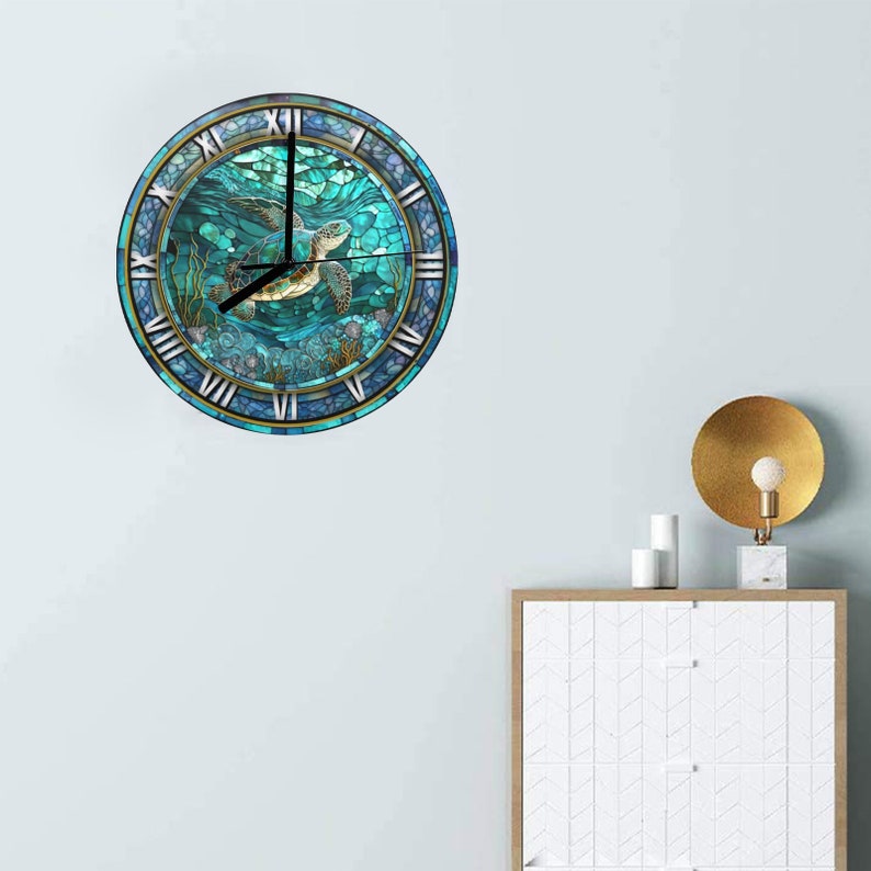 May include: Round wall clock featuring a sea turtle swimming in turquoise water. The clock face has Roman numerals and a decorative border. The clock is mounted on a light blue wall.