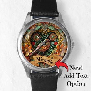 May include: A silver watch with a black leather band. The watch face features a colorful design of a bird in a heart-shaped frame with floral accents. The text "Michelle" is displayed on a banner below the bird.
