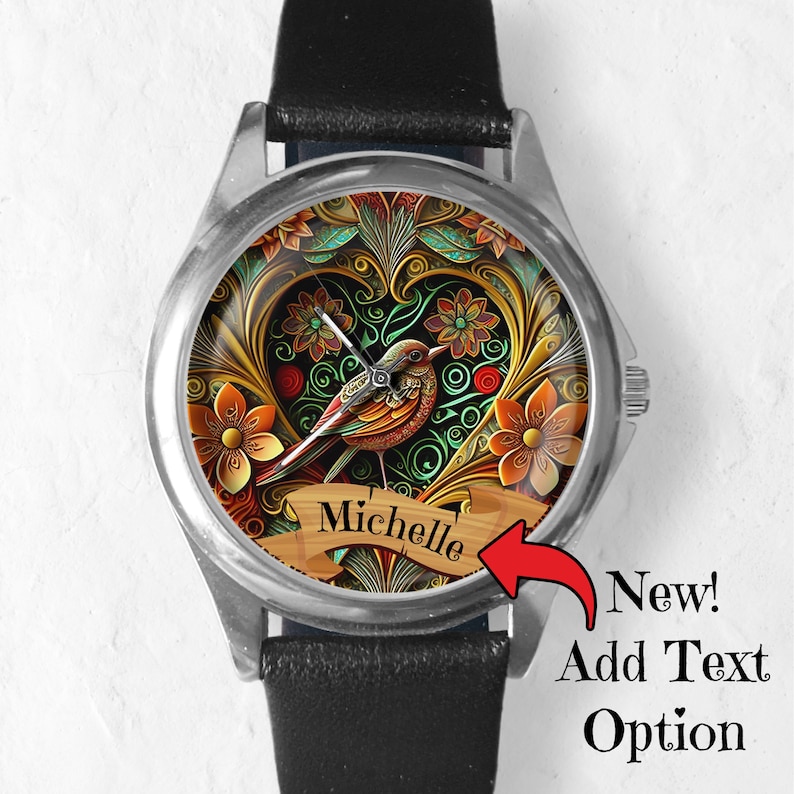 May include: A silver watch with a black leather band. The watch face features a colorful design of a bird in a heart-shaped frame with floral accents. The text "Michelle" is displayed on a banner below the bird.