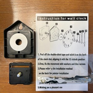 May include: A black wall clock movement kit with instructions. The kit includes a black plastic housing, clock hands, and a paper with instructions for assembly. The instructions are in English.