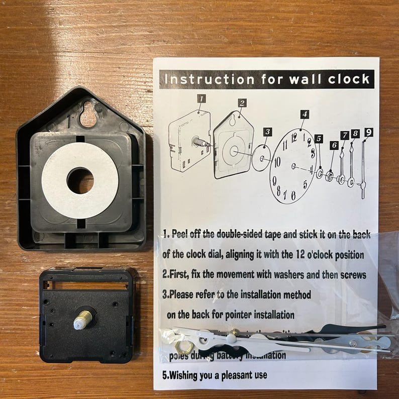 May include: A black wall clock movement kit with instructions. The kit includes a black plastic housing, clock hands, and a paper with instructions for assembly. The instructions are in English.