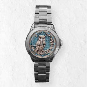May include: A silver wristwatch with an owl design on the face. The owl is brown and beige, set against a blue backdrop within a decorative frame. The watch has a stainless steel strap. The watch face design is approximately 3.5 cm in diameter.