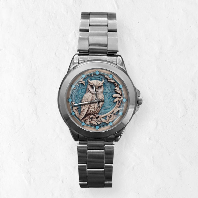 May include: A silver wristwatch with an owl design on the face. The owl is brown and beige, set against a blue backdrop within a decorative frame. The watch has a stainless steel strap. The watch face design is approximately 3.5 cm in diameter.