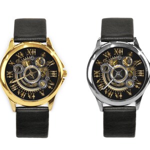 K&ouml;nnte beinhalten: Zwei Armbanduhren mit schwarzen Lederb&auml;ndern. Das Zifferblatt der Uhr links hat ein goldenes Geh&auml;use und das Zifferblatt der Uhr rechts ein silbernes Geh&auml;use. Beide Zifferbl&auml;tter haben einen schwarzen Hintergrund mit goldenen r&ouml;mischen Ziffern f&uuml;r die Stunden und ein detailliertes, kompliziertes, goldfarbenes Zahnrad-Design.