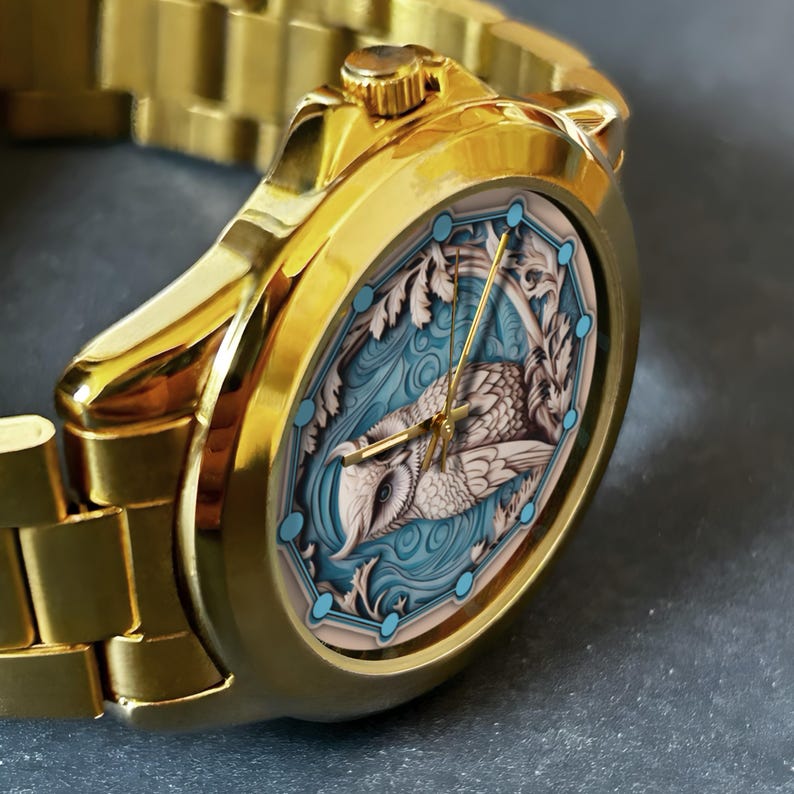 May include: Gold wristwatch with an oval face. The watch face features an owl design in blue, white, and beige. The watch has a gold strap and gold hands. The watch face design is detailed and artistic.