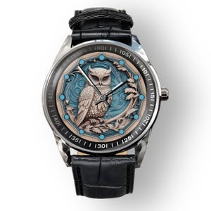 May include: A silver wristwatch with a black leather strap. The watch face features a detailed owl design in white, blue, and beige. The watch has a round face with a black bezel and a textured black leather strap.