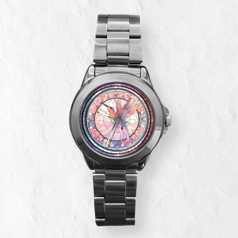 Puede incluir: Un reloj plateado con una correa de acero inoxidable. La esfera del reloj presenta un dise&ntilde;o de vitral colorido de un colibr&iacute; en vuelo.