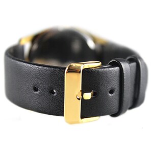 K&ouml;nnte beinhalten: Ein schwarzes Lederarmband mit einer goldenen Schlie&szlig;e. Das Armband hat mehrere L&ouml;cher zum Einstellen der Passform.