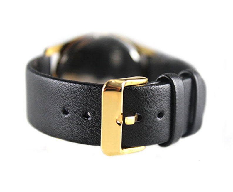 K&ouml;nnte beinhalten: Ein schwarzes Lederarmband mit einer goldenen Schlie&szlig;e. Das Armband hat mehrere L&ouml;cher zum Einstellen der Passform.