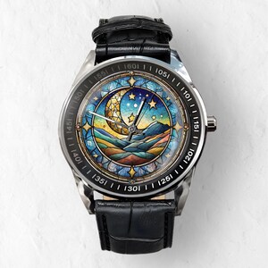 Puede incluir: Un reloj de pulsera plateado con una correa de cuero negro. La esfera del reloj presenta un dise&ntilde;o de vitral con una luna creciente, estrellas y monta&ntilde;as sobre un fondo de cielo azul.
